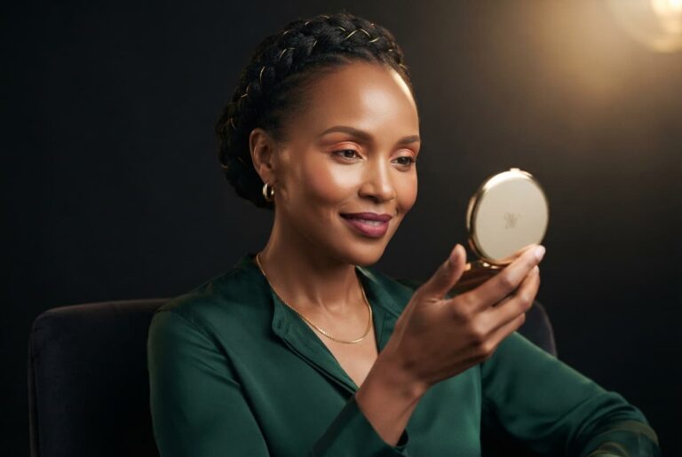 A confident, mature Kenyan woman with smooth features holding a gold compact mirror, representing natural injectables and filler treatments at Luxe Nova Aesthetics.